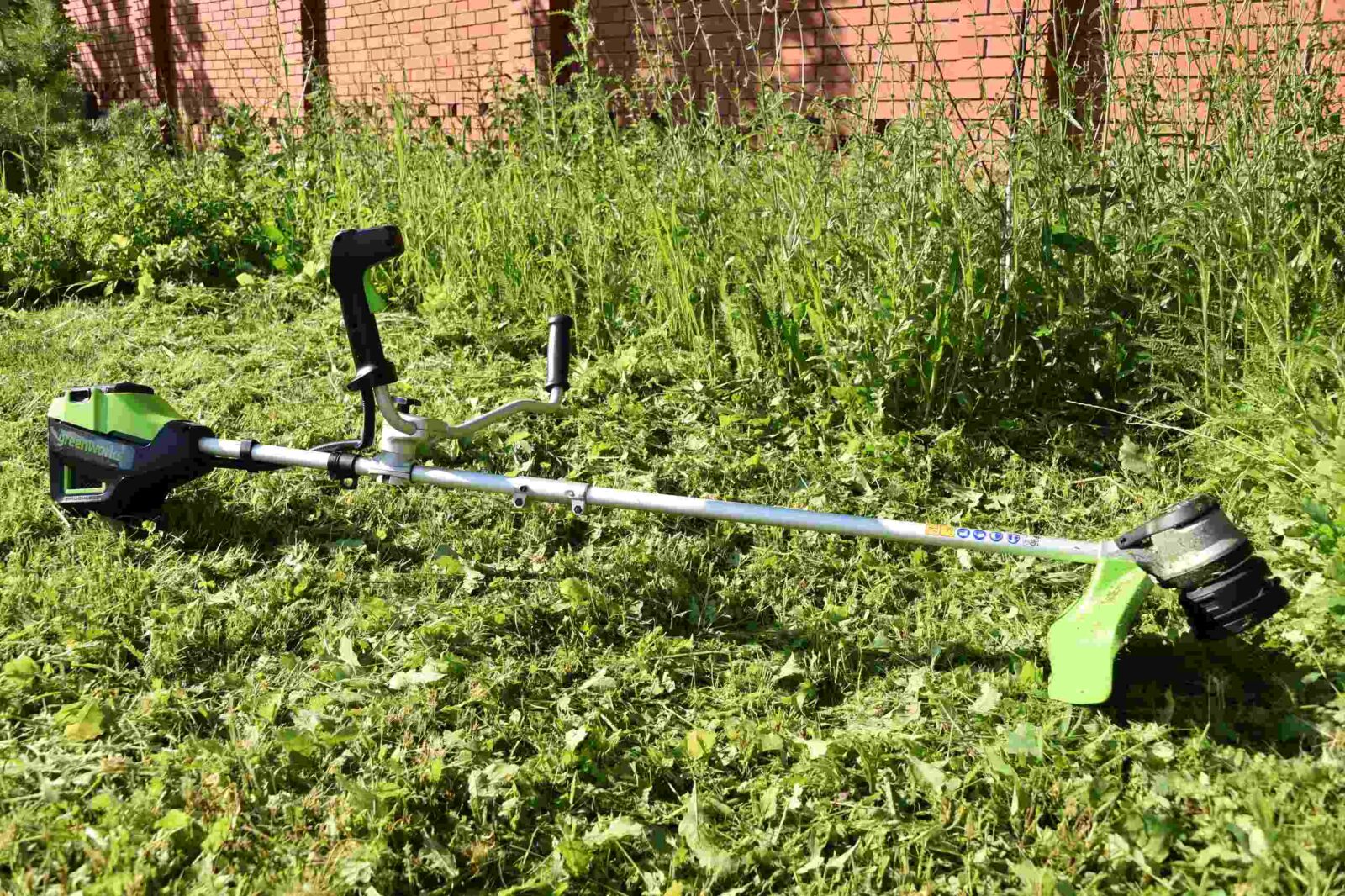 аккумуляторный триммер Greenworks на фоне скошенной травы